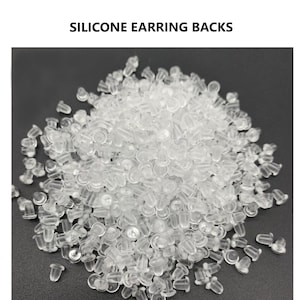 Può includere: Un grande mucchio di supporti per orecchini in silicone trasparente. I supporti sono piccoli e rotondi, con un piccolo perno che sporge dalla parte superiore.