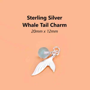 May include: A silver whale tail charm with a light blue bead. The charm is 20mm x 12mm. Text on the image reads "Sterling Silver Whale Tail Charm 20mm x 12mm".
