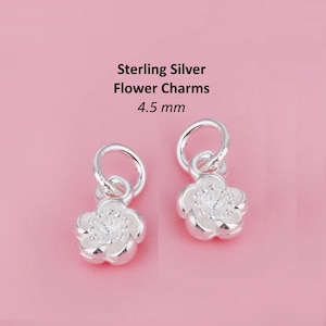 May include: Two sterling silver flower charms with a white enamel finish and a clear rhinestone in the centre. Each charm measures 4.5 mm in diameter.