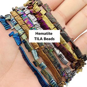 May include: An assortment of multi-coloured hematite TILA beads, featuring metallic hues like blue, gold, silver, and purple. The beads are displayed in rows, highlighting their rectangular form and reflective qualities. The image includes the text "Hematite TILA Beads".