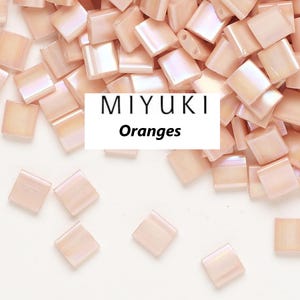 May include: A close-up of a pile of small, square, peach-coloured glass beads with a subtle iridescent sheen. The beads are labelled "MIYUKI Oranges".