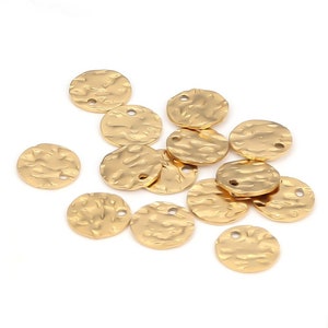 May include: A group of 14 gold-colored metal round charms with a textured surface. Each charm has two small holes at the top.