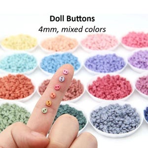 Puede incluir: Surtido de pequeños botones de plástico de 4 mm con dos agujeros, en varios colores pastel. Los botones están dispuestos en cuencos pequeños y una mano sostiene algunos botones para mostrar los colores.
