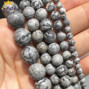 May include: A strand of round, grey and black marbled beads. The beads are various sizes and have a natural, polished look.
