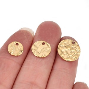 May include: Three gold-colored metal circle charms with a hammered texture and a small hole in the center. The charms are different sizes and are held in a hand.