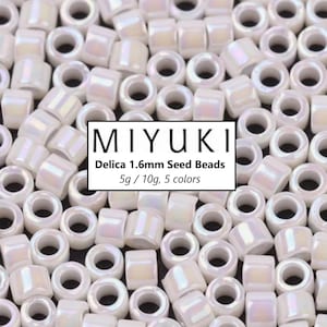 Puede incluir: Primer plano de un montón de cuentas de semillas blancas. Las cuentas son pequeñas y redondas, con un ligero brillo iridiscente. Las cuentas están etiquetadas "MIYUKI Delica 1.6mm Seed Beads 5g / 10g, 5 colores."