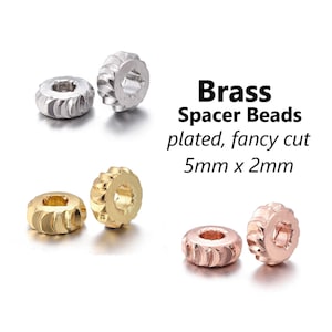 May include: Three sets of brass spacer beads in silver, gold, and rose gold. Each bead is 5mm in diameter and 2mm thick. The beads have a fancy cut design.