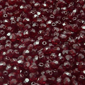 May include: A close-up shot of numerous dark red, faceted beads. The beads are closely packed, displaying a textured surface. Each bead has multiple facets, reflecting light and creating highlights. The beads are suitable for jewellery making.