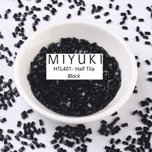 May include: A bowl filled with black Miyuki seed beads, labelled "HTL401 - Half Tila Black".