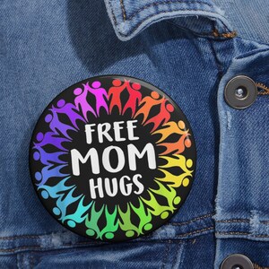 May include: A black button with a rainbow circle of people holding hands around the text "FREE MOM HUGS".