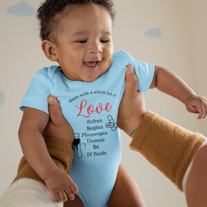 Puede incluir: Un bebé con un body azul claro con el texto "made with a whole lot of Love" y una lista de medicamentos: Zofran, Reglan, Phenergan, Unisom, B6, IV fluids.