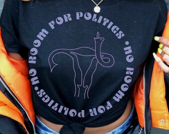 Könnte beinhalten: Schwarzes T-Shirt mit einer lila Umrandung einer Gebärmutter und dem Text "No room for politics * no room for politics" darum herum.