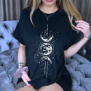 May include: Black t-shirt with a white moon and stars graphic. The graphic features three moons in different phases, a starburst, and a vertical arrow.