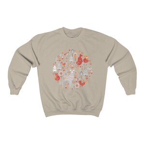 May include: A beige sweatshirt with a circular design featuring a deer, birds, trees, and flowers in shades of red, orange, and blue.