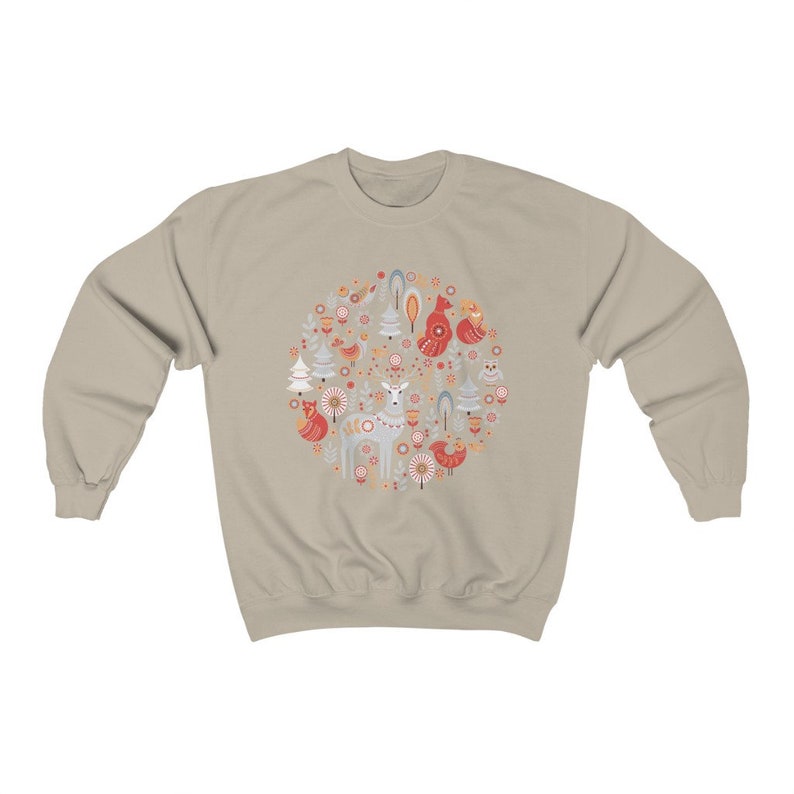 May include: A beige sweatshirt with a circular design featuring a deer, birds, trees, and flowers in shades of red, orange, and blue.