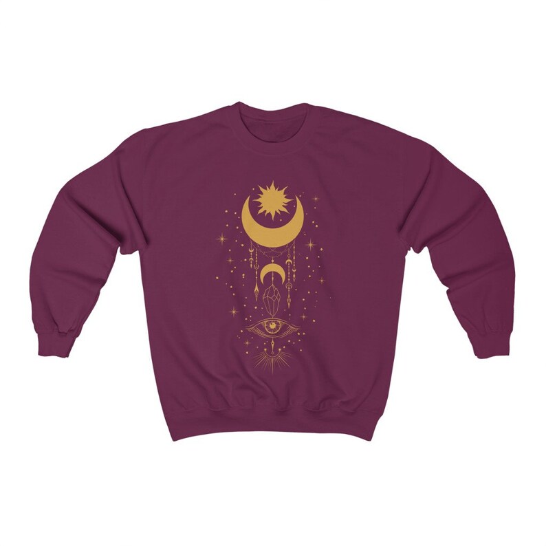 May include: Burgundy sweatshirt with a gold celestial design featuring a crescent moon, sun, stars, and an eye.
