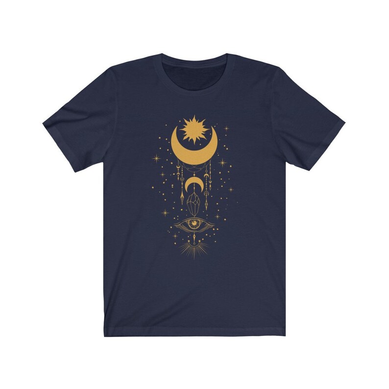 May include: A navy blue t-shirt with a gold crescent moon, sun, and eye design. The design features a crescent moon with a sun inside, a dangling eye, and stars.