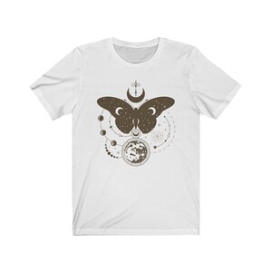May include: White t-shirt with a brown butterfly design. The butterfly is surrounded by a circle of moons and stars.