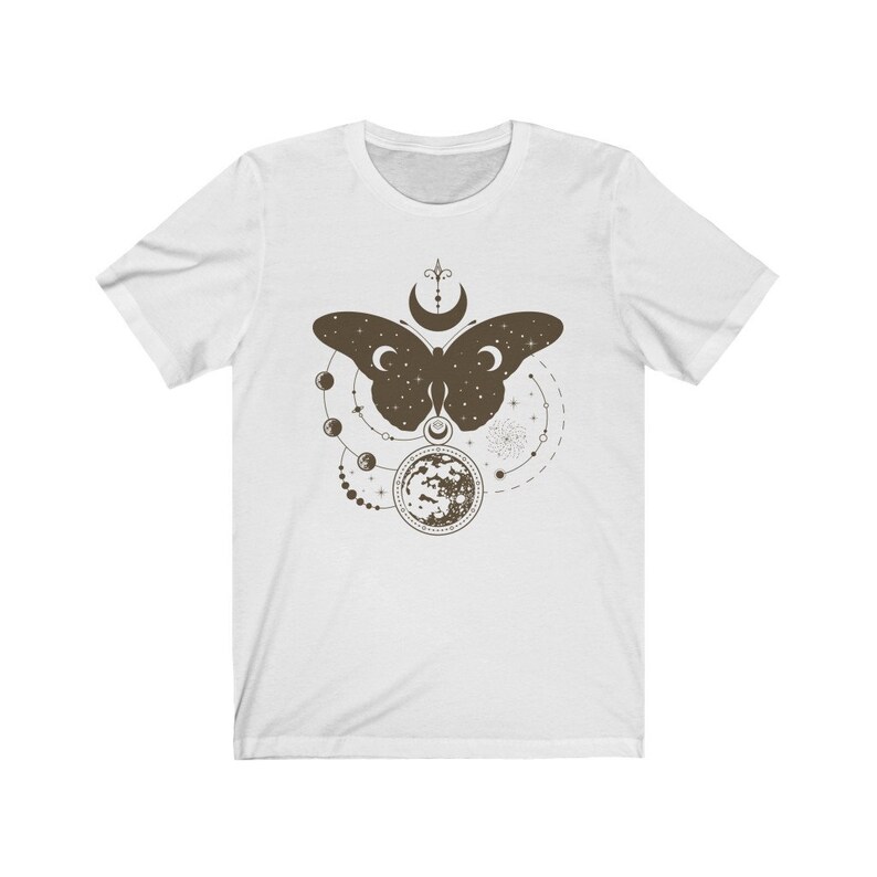May include: White t-shirt with a brown butterfly design. The butterfly is surrounded by a circle of moons and stars.