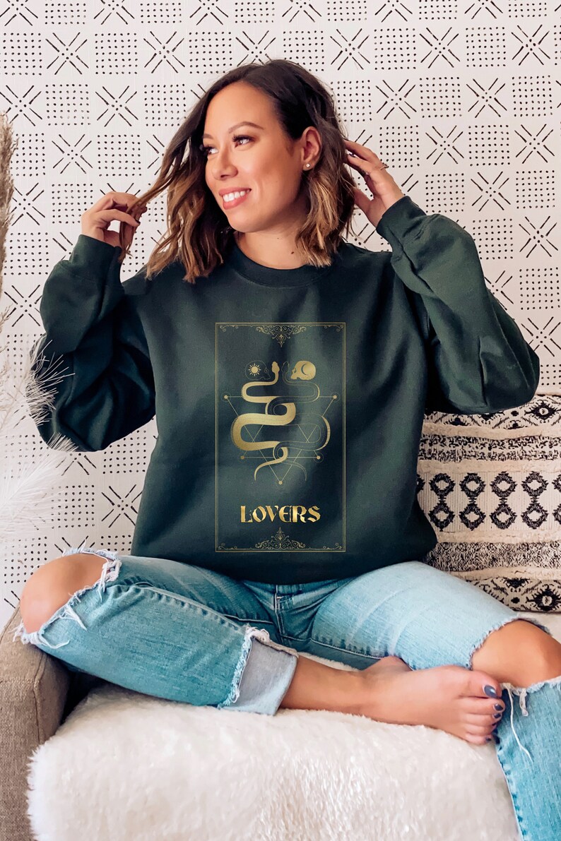 Puede incluir: Una sudadera verde oscuro con un gr&aacute;fico dorado de una serpiente y la palabra "LOVERS" en la parte delantera.