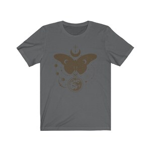 May include: A dark gray t-shirt with a brown graphic of a butterfly with a moon and stars. The butterfly is surrounded by a circle of small moons and stars.
