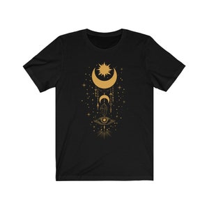 May include: Black t-shirt with a gold design of a crescent moon, sun, stars, and an eye with a crystal pendant.