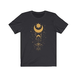May include: A black t-shirt with a gold design of a crescent moon, sun, and eye with geometric shapes and stars.