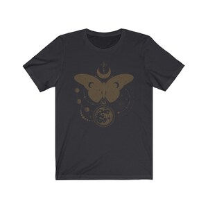 May include: A dark gray t-shirt with a gold-colored design of a butterfly with a crescent moon and stars. The design is centered on the shirt.