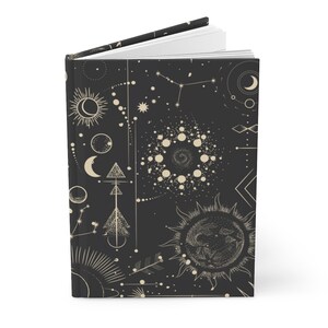 May include: A black journal with a gold celestial pattern. The pattern includes moons, stars, suns, and geometric shapes.