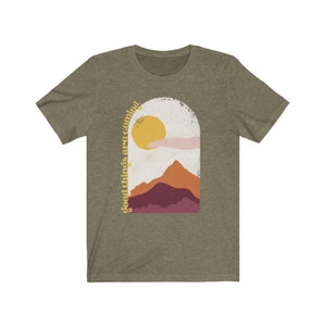 Puede incluir: Una camiseta verde con un gr&aacute;fico de una cordillera y un sol con el texto "good things are coming" en una fuente retro.