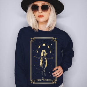 Op de afbeelding: Een marineblauw sweatshirt met een gouden afbeelding van de Hogepriesteres tarotkaart. De kaart toont een vrouw met een slang om haar heen, die voor een halve maan en sterren staat.
