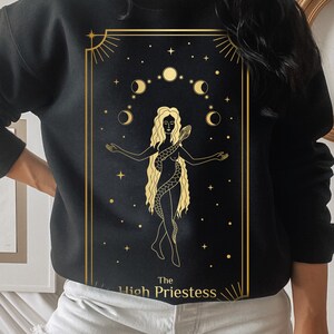 Op de afbeelding: Zwart sweatshirt met een gouden afbeelding van de Hogepriesteres tarotkaart. De kaart toont een vrouw met een slang en halve manen.