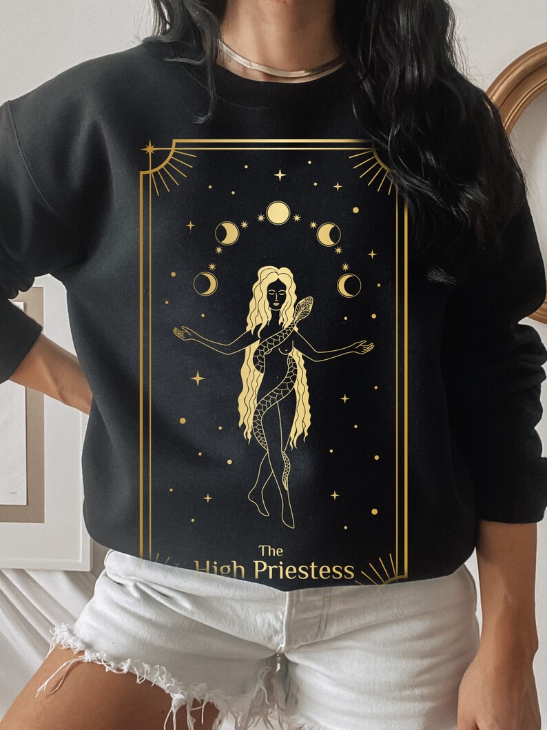 Op de afbeelding: Zwart sweatshirt met een gouden afbeelding van de Hogepriesteres tarotkaart. De kaart toont een vrouw met een slang en halve manen.