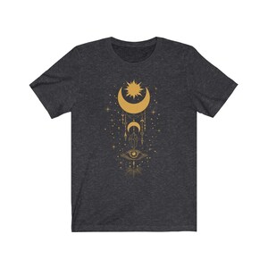 May include: A dark heather grey t-shirt with a gold celestial design featuring a crescent moon, sun, stars, and an eye.