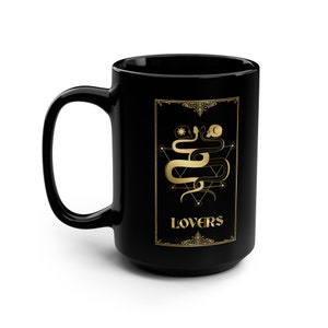 Puede incluir: Taza de caf&eacute; de cer&aacute;mica negra con un dise&ntilde;o dorado de dos serpientes entrelazadas alrededor de un pentagrama con la palabra "LOVERS" en letras doradas.