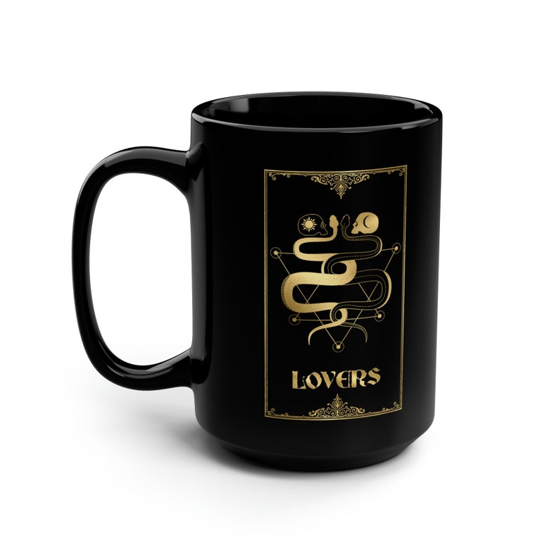 Puede incluir: Taza de caf&eacute; de cer&aacute;mica negra con un dise&ntilde;o dorado de dos serpientes entrelazadas alrededor de un pentagrama con la palabra "LOVERS" en letras doradas.