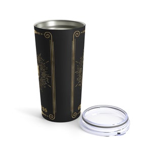 May include: A black stainless steel tumbler with a gold design featuring a sunburst and the word "Happiness". The tumbler has a clear lid.