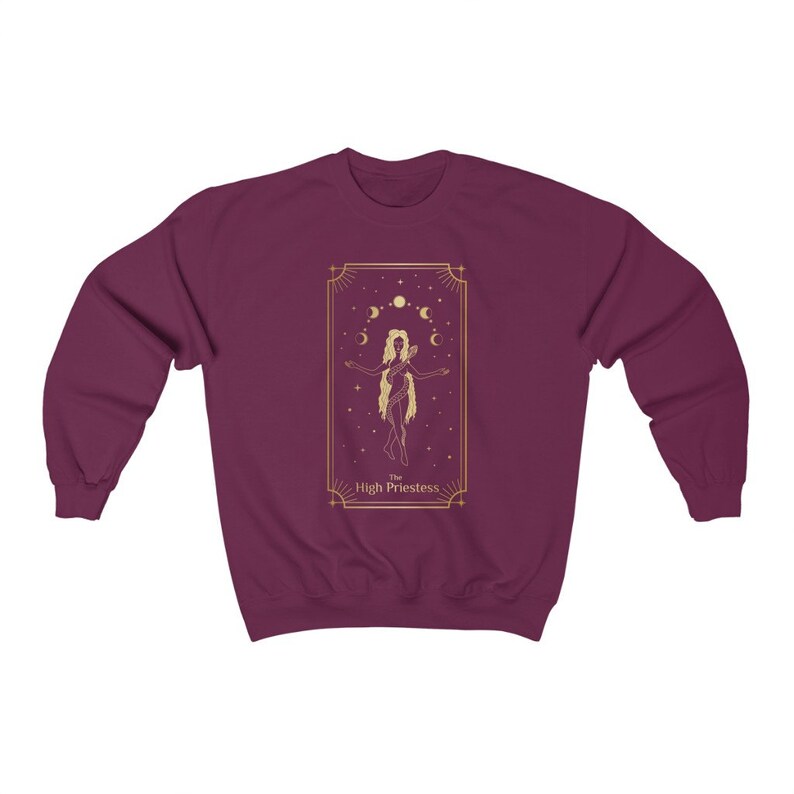 Op de afbeelding: Een bordeauxrood sweatshirt met een gouden afbeelding van de Hogepriesteres tarotkaart. De kaart toont een vrouw die met haar armen gespreid staat, omringd door manen en sterren.