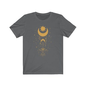 May include: A dark gray t-shirt with a gold design of a crescent moon, sun, and eye with geometric shapes and stars.