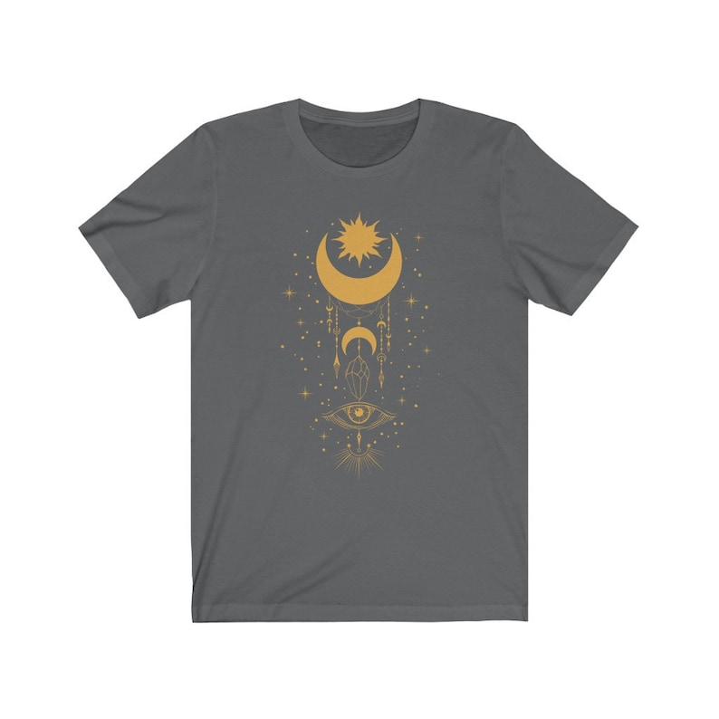May include: A dark gray t-shirt with a gold design of a crescent moon, sun, and eye with geometric shapes and stars.