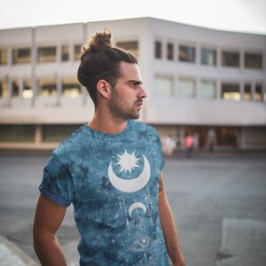 May include: A blue tie-dye t-shirt with a white moon and star design. The design also includes a stylized eye and other celestial symbols.