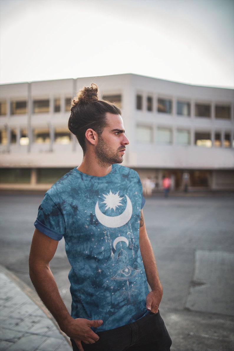 May include: A blue tie-dye t-shirt with a white moon and star design. The design also includes a stylized eye and other celestial symbols.