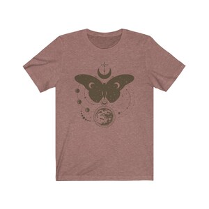 May include: A heather gray t-shirt with a brown butterfly design. The butterfly is surrounded by a circle of moons and stars.