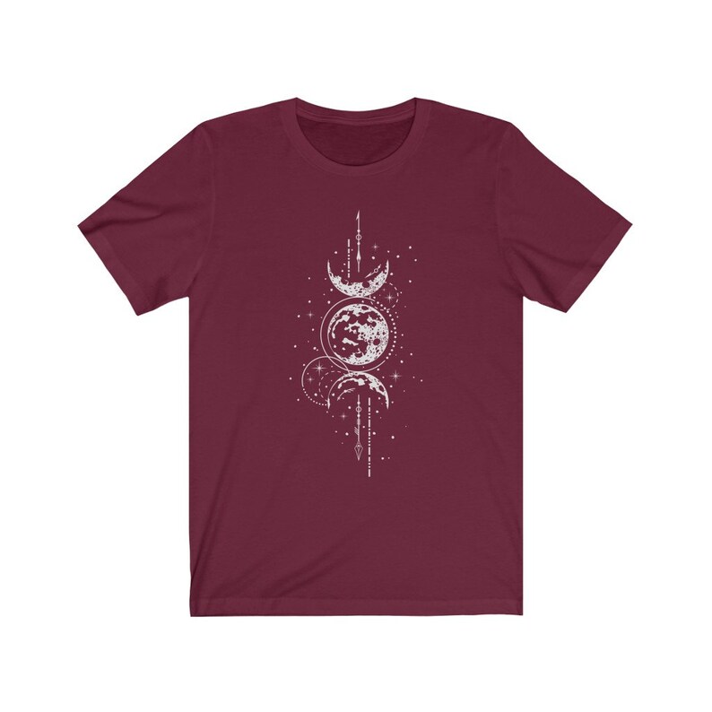 May include: A maroon t-shirt with a white graphic of three moons and stars. The moons are in different phases and are connected by a line of stars.