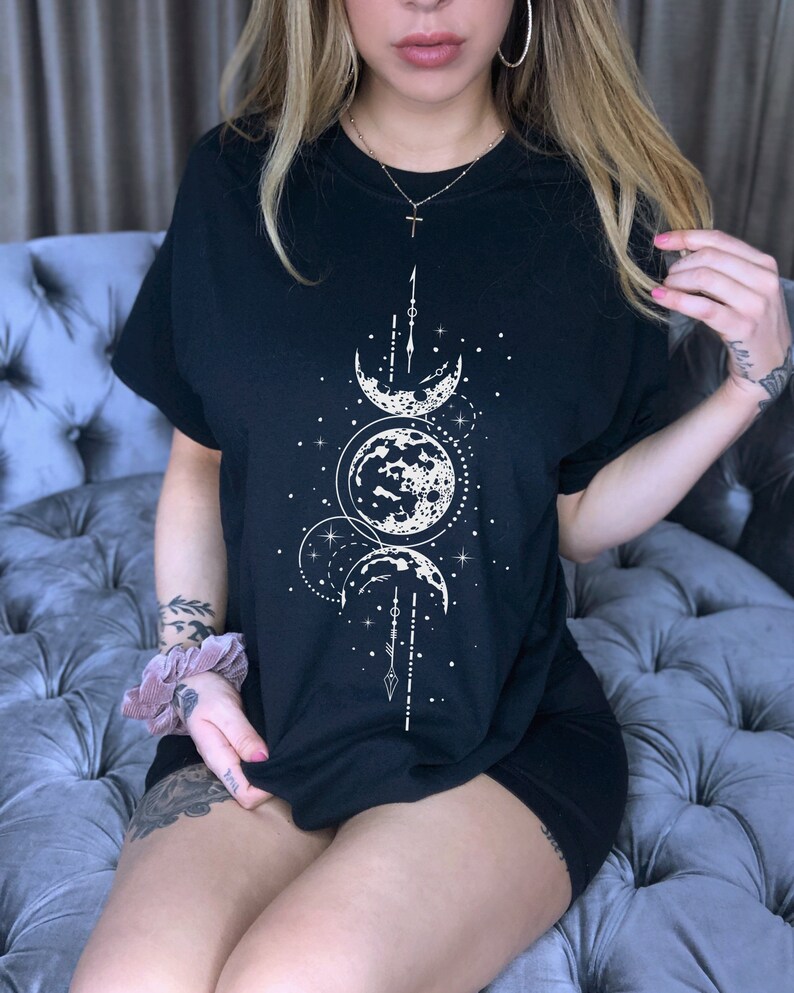 May include: Black t-shirt with a white moon and stars graphic. The graphic features three moons in different phases, a starburst, and a vertical arrow.