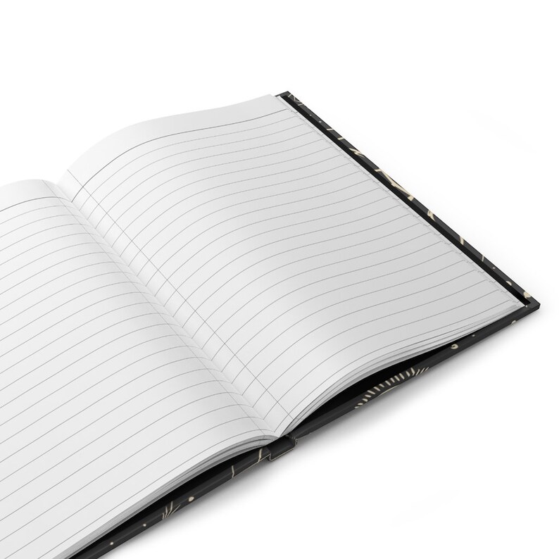 May include: An open notebook with lined pages and a black cover with a gold pattern. The notebook is lying open on a white surface.