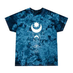 May include: A blue tie-dye t-shirt with a white graphic of a crescent moon, sun, and eye with geometric designs. The graphic is centered on the shirt.