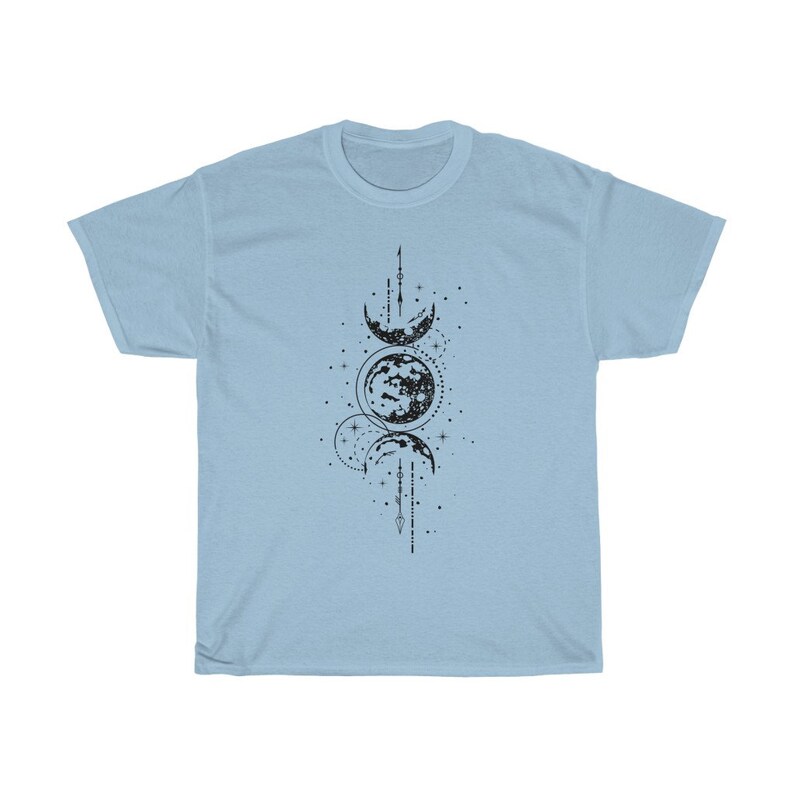 May include: Light blue t-shirt featuring a black graphic of a celestial design. The design includes phases of the moon, stars, and geometric lines. The shirt is made of a soft material.