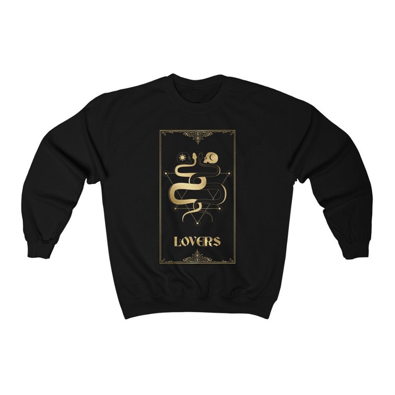 Puede incluir: Sudadera negra con un dise&ntilde;o dorado de una serpiente con un sol y una luna encima. El dise&ntilde;o est&aacute; en un marco con la palabra "LOVERS" debajo.