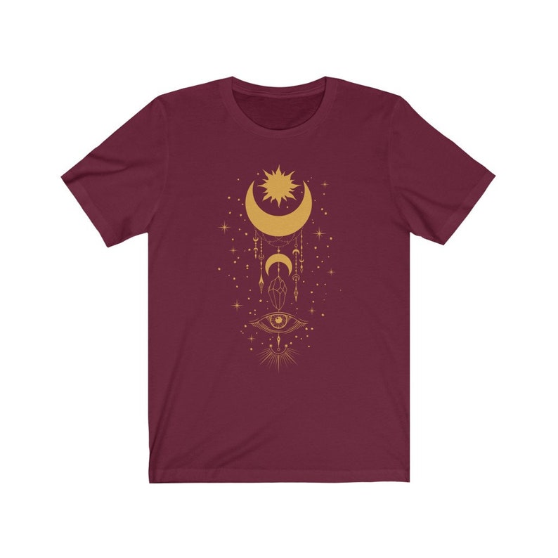 May include: A maroon t-shirt with a gold design of a crescent moon, sun, eye, and other celestial symbols.